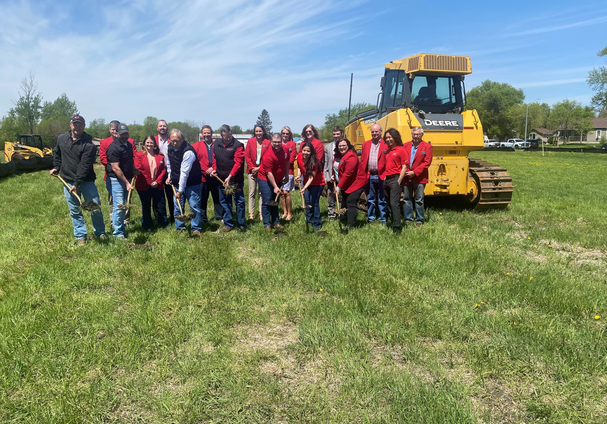 group of people digging on green grass with shovels and a yellow tractor in the background